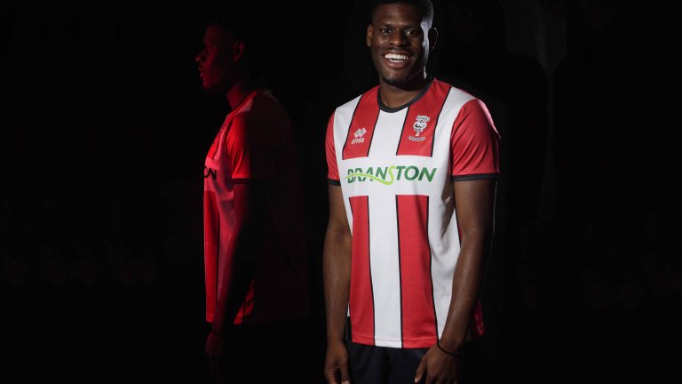 Chris Vaughan Photography - commercial photography | An image of Lincoln City&rsquo;s TJ Eyoma modelling a clubs red and white shirt. The image is shot against a black background and features a multiple exposure with a side on image of TJ illuminated in red lighting.