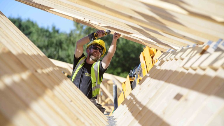Chris Vaughan Photography - commercial photography | The woodwork of a house being built creates a triangle shape as it frames a construction worker who is working on the development.