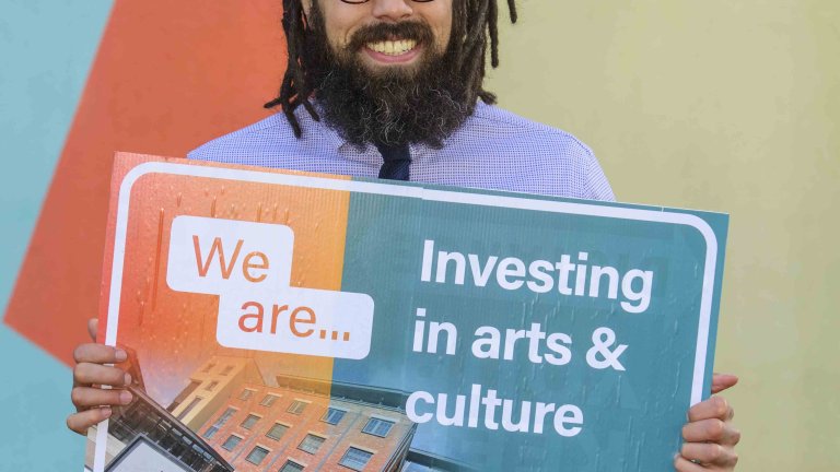 Chris Vaughan Photography - commercial photography | A member of staff holds a board reading “Investing in arts & culture”.