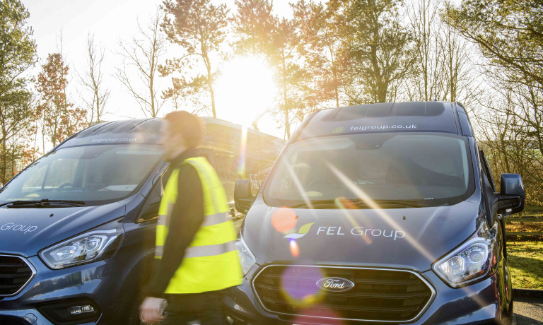 Chris Vaughan Photography - commercial photography | Sunlight breaks through the image as a worker in high-vis walks past his companies vans.