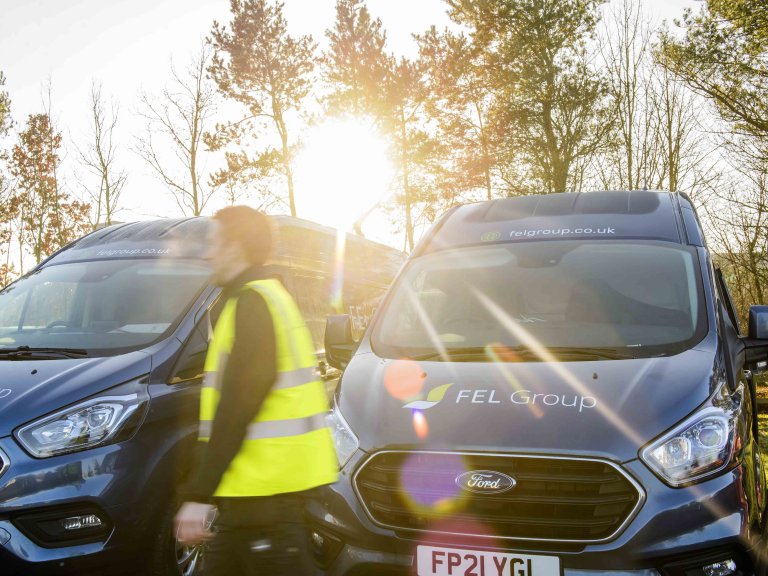 Chris Vaughan Photography - commercial photography | Sunlight breaks through the image as a worker in high-vis walks past his companies vans.