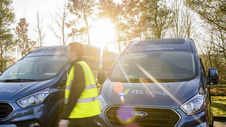 Chris Vaughan Photography - commercial photography | Sunlight breaks through the image as a worker in high-vis walks past his companies vans.