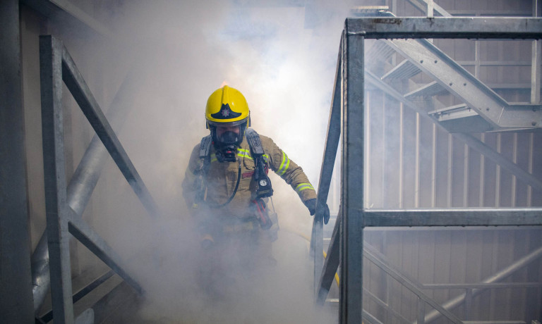 An image of a firefighter walking up stairs in a smoke-filled room during a training exercise.