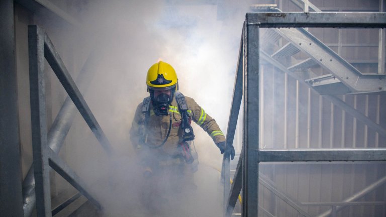 An image of a firefighter walking up stairs in a smoke-filled room during a training exercise.