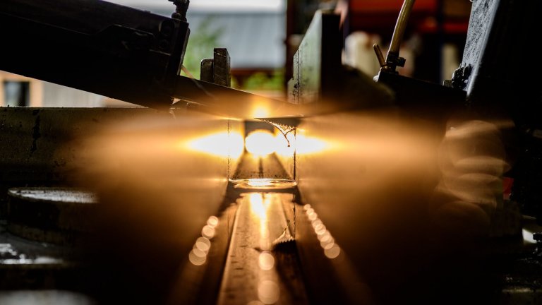 An image of a saw cutting through a metal tube as light shines through illuminating drops of water used to keep the saw cool.