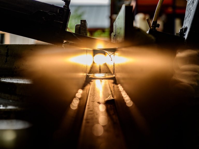 An image of a saw cutting through a metal tube as light shines through illuminating drops of water used to keep the saw cool.