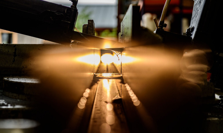 An image of a saw cutting through a metal tube as light shines through illuminating drops of water used to keep the saw cool.