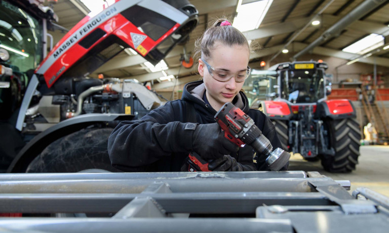 A female engineer used a hand tool infront of a Massey Ferguson tractor.