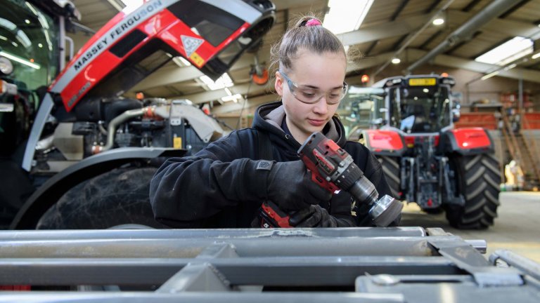 A female engineer used a hand tool infront of a Massey Ferguson tractor.