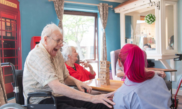 A care home resident, sat in a wheelchair, jokes with a carer.