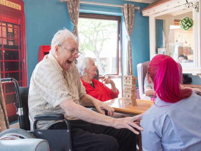 A care home resident, sat in a wheelchair, jokes with a carer.