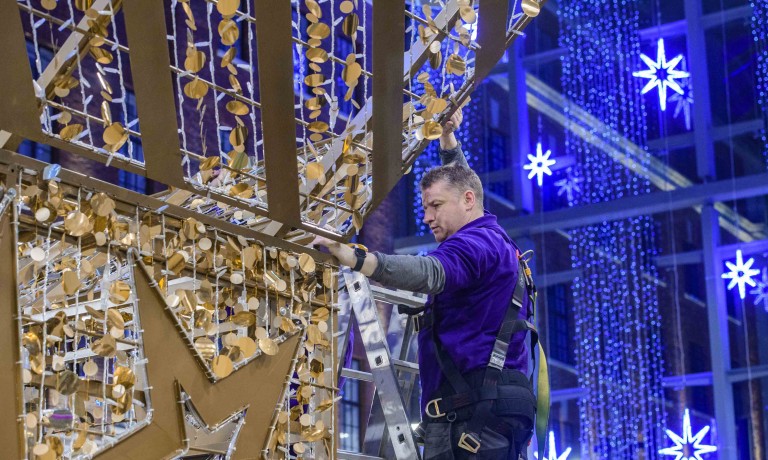 Chris Vaughan Photography - commercial photography | A worker installs gold star Christmas decorations in a shopping centre.