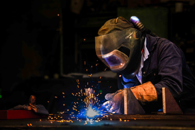 A worker, wearing full PPE welding. Sparks are visible from the area they are welding.