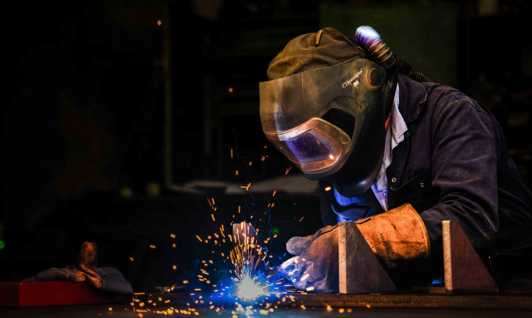 A worker, wearing full PPE welding. Sparks are visible from the area they are welding.