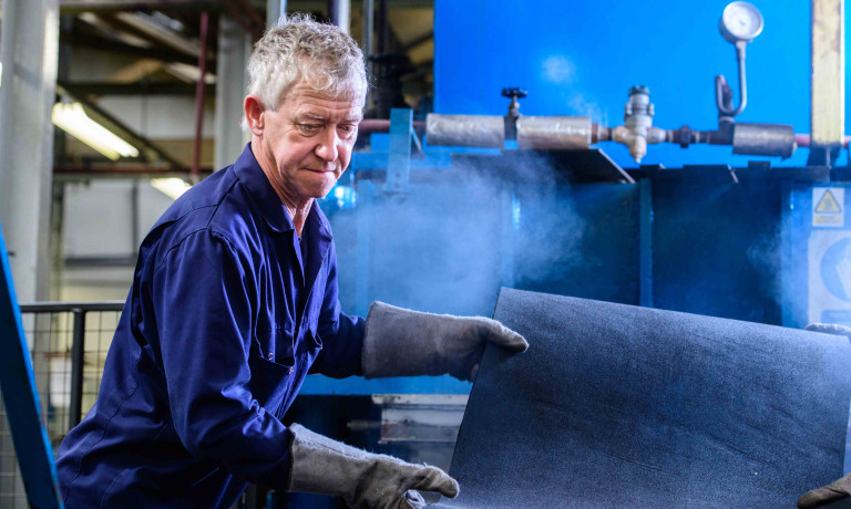 Chris Vaughan Photography - commercial photography | A worker in blue overalls adjusts a piece of material as he works at his machine.