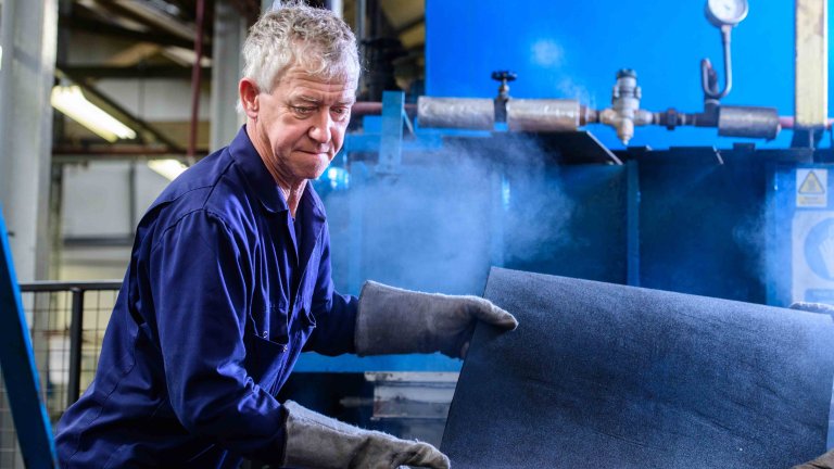 Chris Vaughan Photography - commercial photography | A worker in blue overalls adjusts a piece of material as he works at his machine.