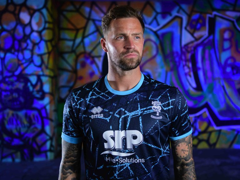 Chris Vaughan Photography - commercial photography | A Lincoln City player models the clubs blue away kit. He is photographed against graffiti which is illuminated with blue light.