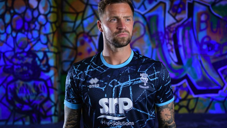 Chris Vaughan Photography - commercial photography | A Lincoln City player models the clubs blue away kit. He is photographed against graffiti which is illuminated with blue light.