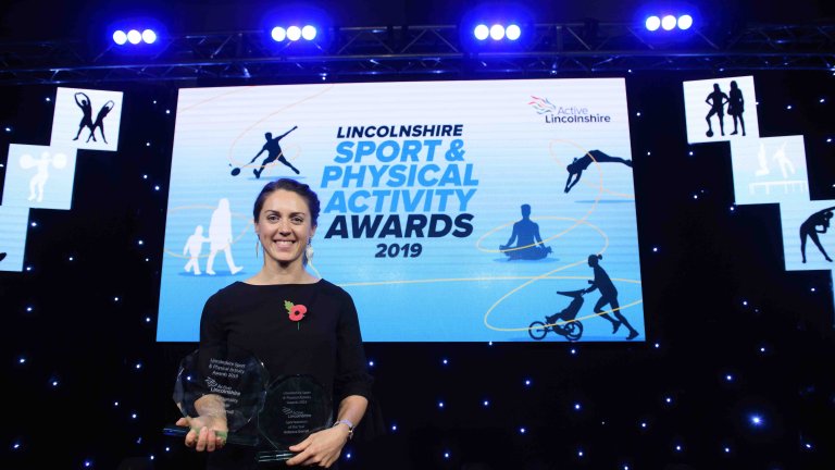 Chris Vaughan Photography - corporate event images | An award recipient stands with their awards on stage in front of the events branding on the big screen.