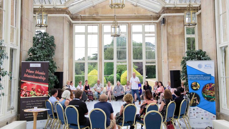Chris Vaughan Photography - corporate event images | A speaker stands talking to a group of delegates who are sat on chairs in a circle around him during a conference.