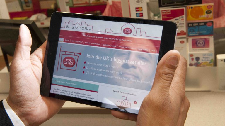 Chris Vaughan Photography - PR and communications images | The face of a postmaster is reflected in an iPad screen which shows the Run a Post Office website.