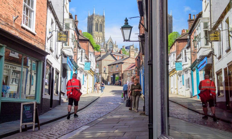 An image of a postman during his delivery walking up Steep Hill Lincoln towards Lincoln Cathedral.