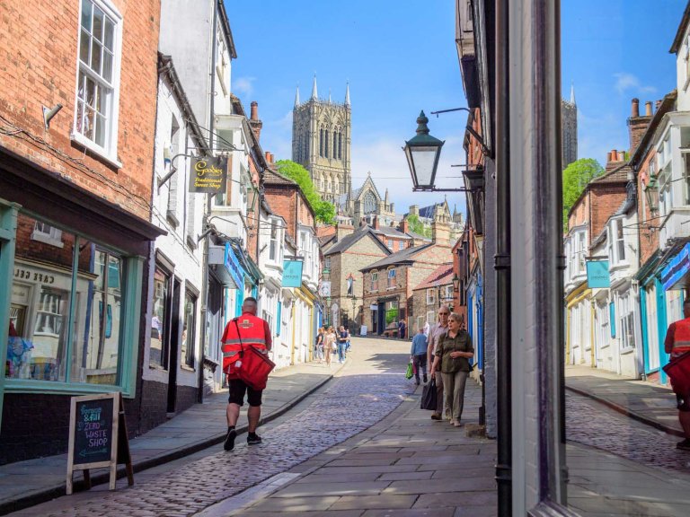 An image of a postman during his delivery walking up Steep Hill Lincoln towards Lincoln Cathedral.