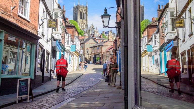An image of a postman during his delivery walking up Steep Hill Lincoln towards Lincoln Cathedral.