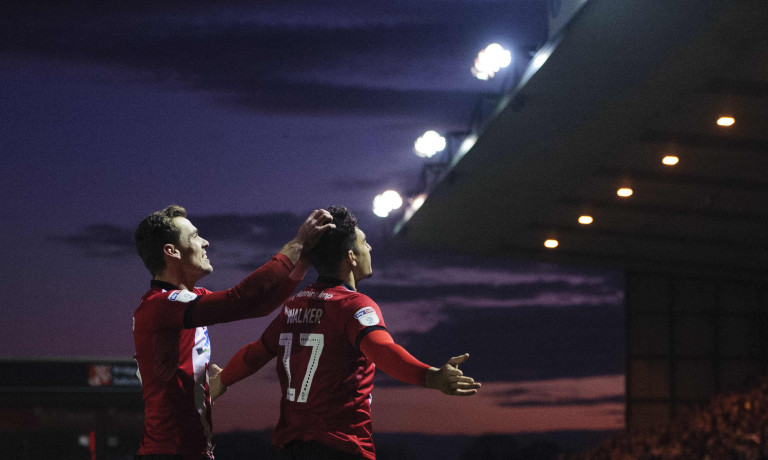 Chris Vaughan Photography - Sports images | Lincoln City players Harry Toffolo and Tyler Walker celebrate a goal as the sun sets in the background.