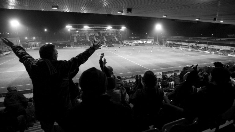 Chris Vaughan Photography - Sports images | A black and white picture taken from the back of a stand as football fans react to a decision.