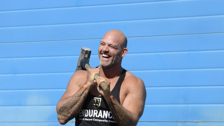Chris Vaughan Photography - commercial photography | Former TV Gladiator, Hunter, stands holding a sledgehammer during filming of an advert for a door manufacturer.