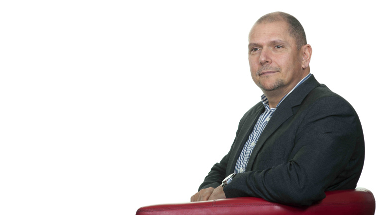 Chris Vaughan Photography - Business profile images | Business coach, Simon Meadows of Sterling Business Coaching, looks off camera as he sits in a chair. He is photographed against a white studio background.