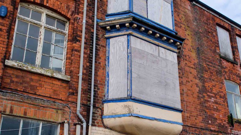 Front elevation of Building 89 with boarded windows and its distinctive enclosed bay window.