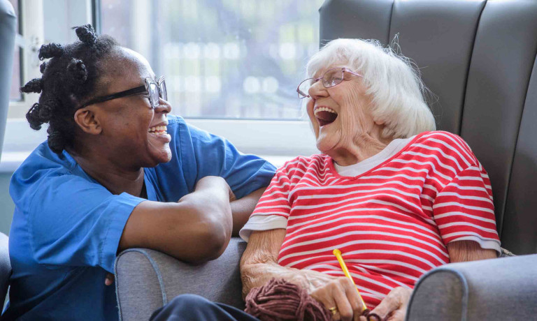 A care worker kneels next to a resident in a care home as they share a joke.