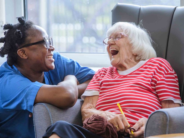 A care worker kneels next to a resident in a care home as they share a joke.