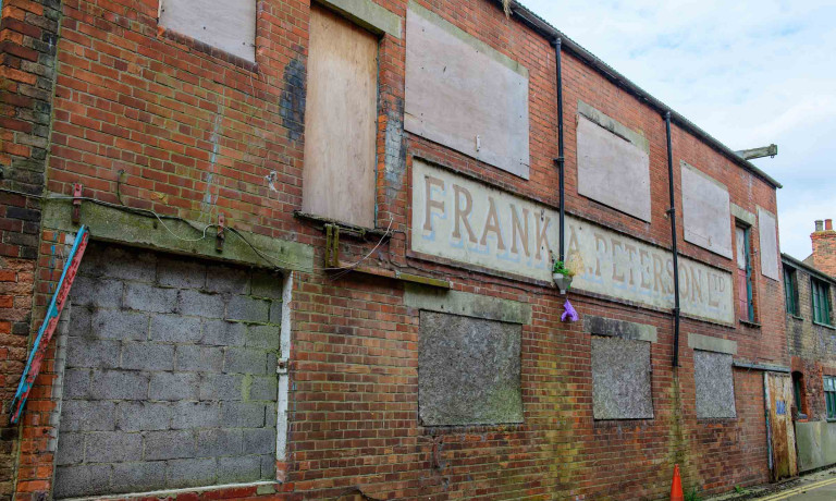 Boarded red-brick frontage of Peterson&rsquo;s Smokehouse with its faded painted company sign.