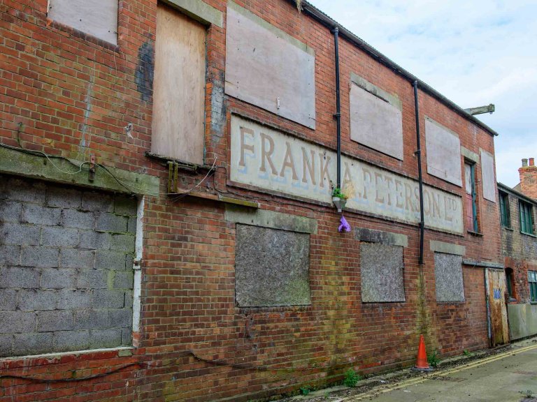 Boarded red-brick frontage of Peterson&rsquo;s Smokehouse with its faded painted company sign.