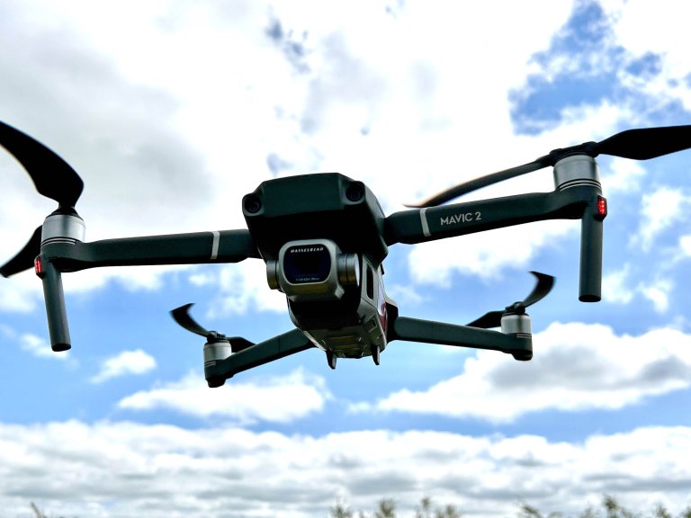 An image of a DJI Mavic 2 Pro hovering against a sunny blue sky filled with white clouds.