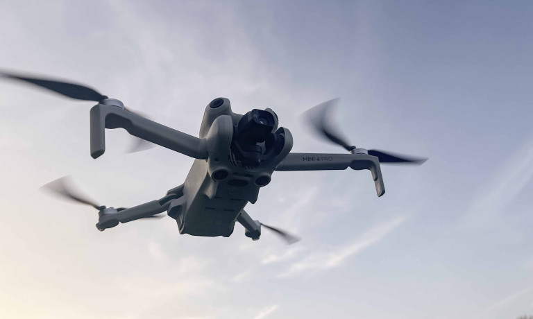 A DJI Mini 4 Pro hovering with the sky in the background.