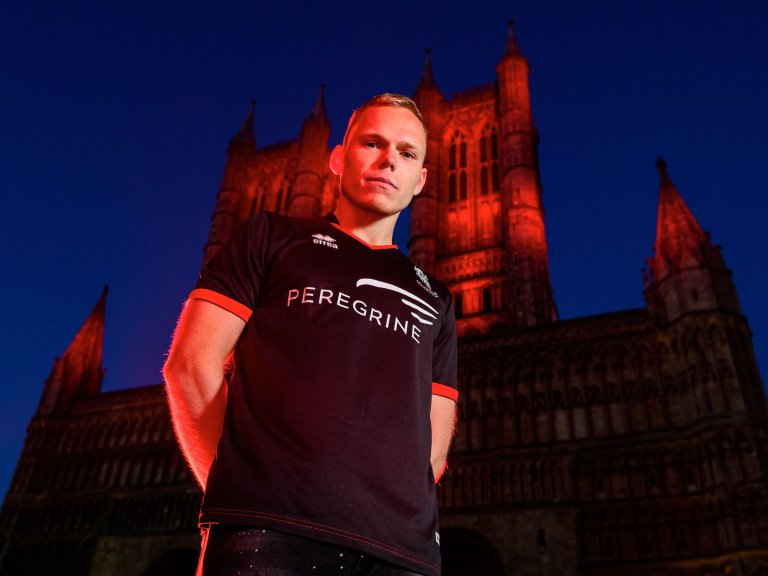 Anthony Scully wearing the 2020/21 Lincoln City black away kit with Lincoln Cathedral illuminated red behind him.