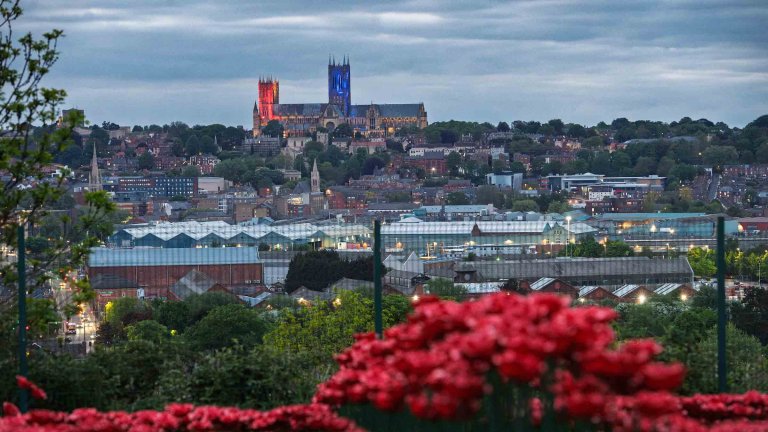 The view past ceramic poppies at IBCC towards Lincoln Cathedral which is lit in red, white and blue to mark VE Day 80.