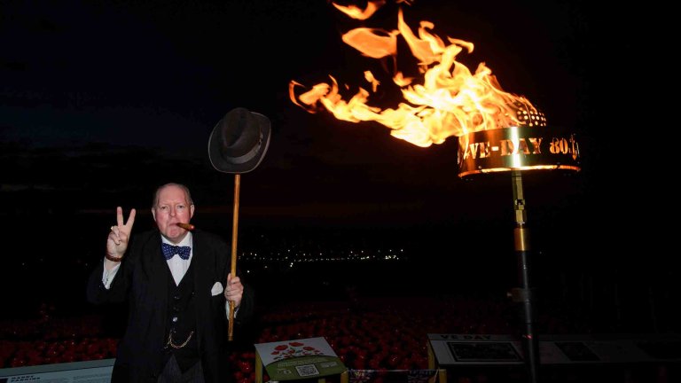 A Winston Churchill re-enactor stands next to a beacon lit on the 80th anniversary of VE Day.