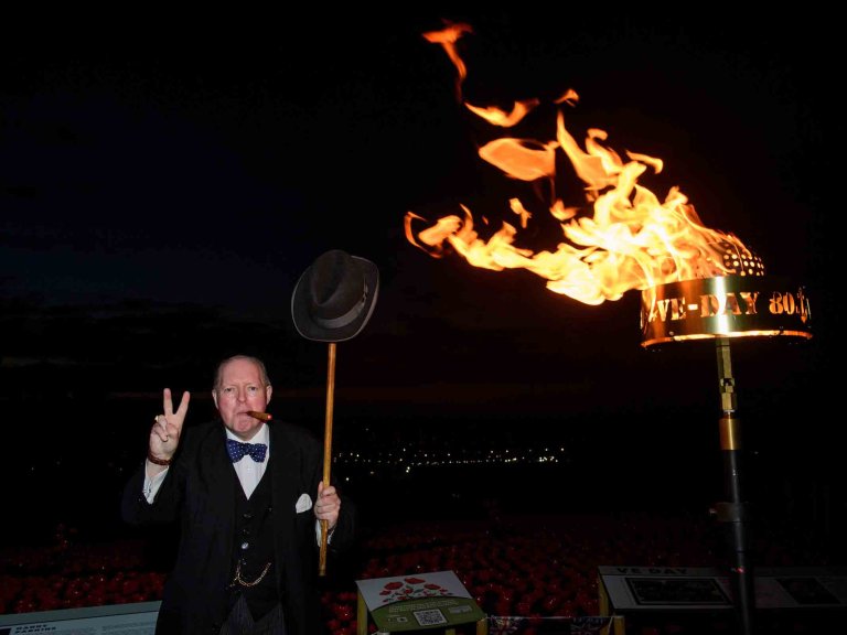 A Winston Churchill re-enactor stands next to a beacon lit on the 80th anniversary of VE Day.