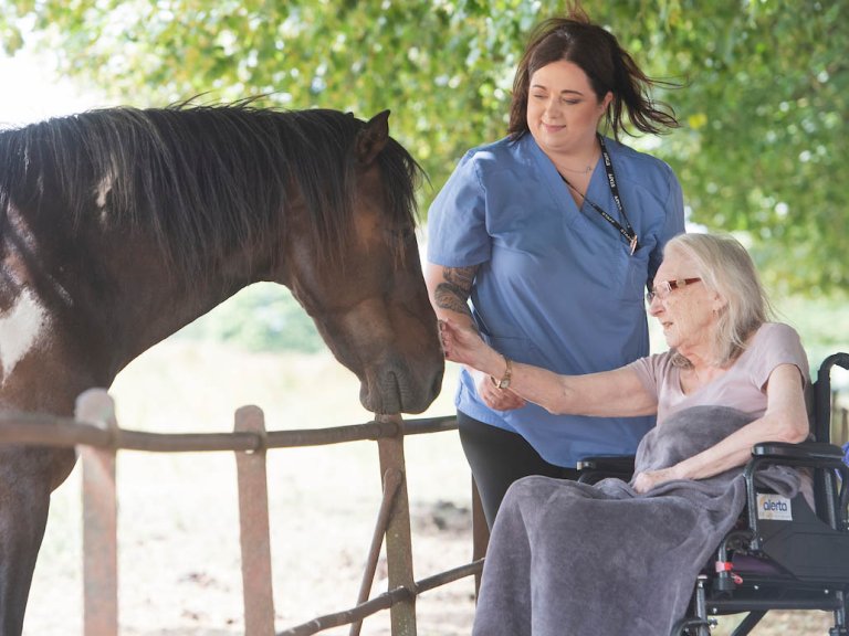 A resident and carer fussing a horse whilst out for a walk.