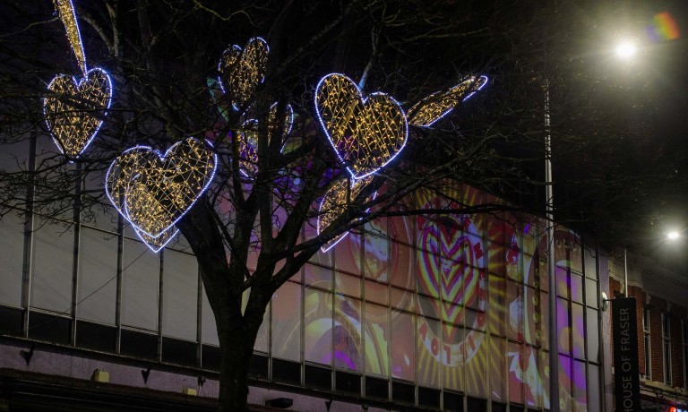 Illuminated hearts are seen in a tree, whilst projections of love hearth illuminate the side of a department store.