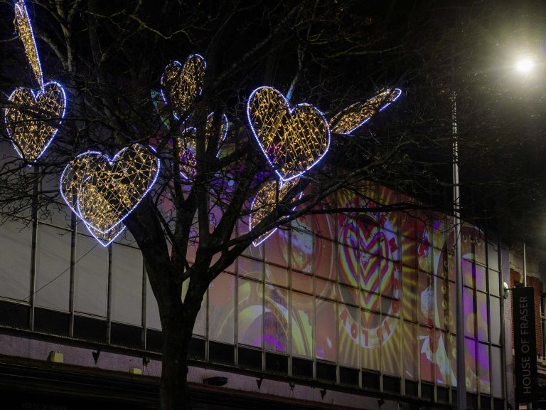 Illuminated hearts are seen in a tree, whilst projections of love hearth illuminate the side of a department store.