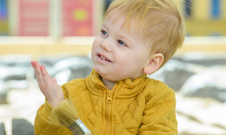 A young child explores a dinosaur dig pit.