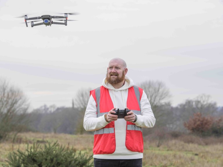 A profile picture of Chris Vaughan, owner of Chris Vaughan Photography, flying a drone. Chris is wearing a white hoodie and a high-vis jacket that has drone pilot written on the back.