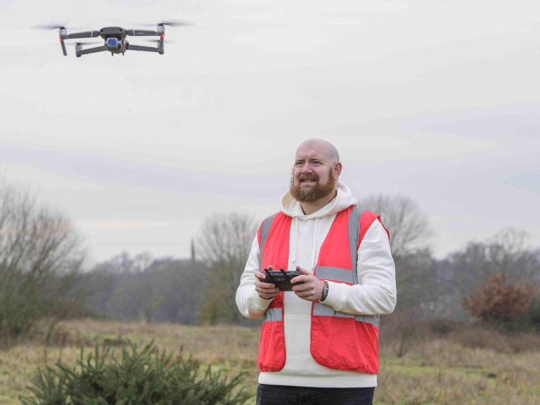 A profile picture of Chris Vaughan, owner of Chris Vaughan Photography, flying a drone. Chris is wearing a white hoodie and a high-vis jacket that has drone pilot written on the back.
