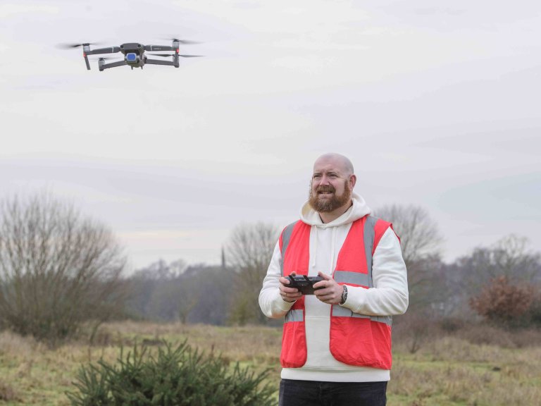 A profile picture of Chris Vaughan, owner of Chris Vaughan Photography, flying a drone. Chris is wearing a white hoodie and a high-vis jacket that has drone pilot written on the back.